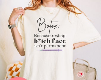 Może przedstawiać: Biały t-shirt z napisem "Botox: Because resting b*tch face isn't permanent" i grafiką fioletowej i białej strzykawki. Słowo "Naturalny" jest napisane różowym kolorem na białym tle.