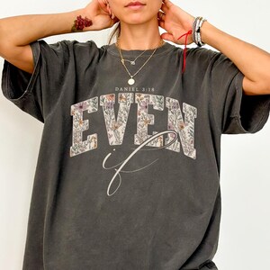 Puede incluir: Camiseta gris oscuro con el texto "EVEN if" en un dise&ntilde;o floral. El texto "DANIEL 3:18" est&aacute; encima de la palabra "EVEN". La camiseta tiene un aspecto vintage y desgastado.