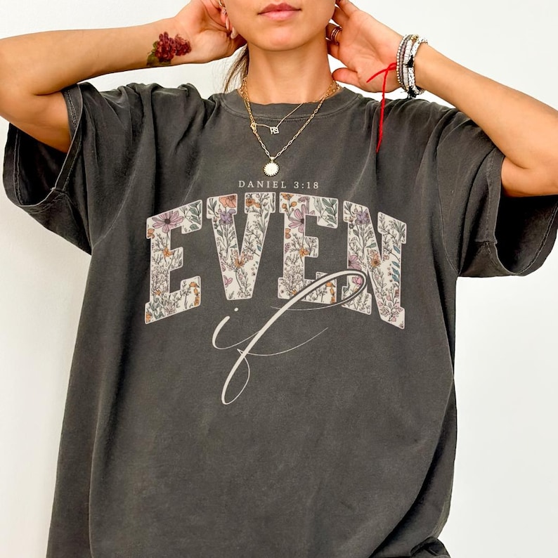 Puede incluir: Camiseta gris oscuro con el texto "EVEN if" en un dise&ntilde;o floral. El texto "DANIEL 3:18" est&aacute; encima de la palabra "EVEN". La camiseta tiene un aspecto vintage y desgastado.