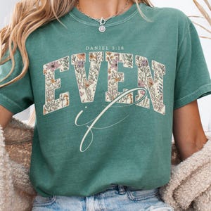 Puede incluir: Una camiseta verde azulado con las palabras "EVEN if" en un dise&ntilde;o floral. El texto "DANIEL 3:18" est&aacute; encima de la palabra "EVEN". La camiseta es de cuello redondo y tiene mangas cortas.