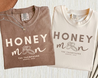 May include: Two t-shirts with the text "Honeymoon" and a stylised ring design. The brown t-shirt has the text "THE THOMPSONS GREECE, 2025" and the beige t-shirt has the text "THE THOMPSONS GREECE, 2025".