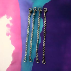May include: Four silver chain extenders with lobster claw clasps. The chains are hanging against a pink, blue, and purple background.