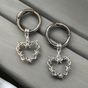 May include: Two silver keychains with a barbed wire heart charm. The keychains are made of metal and have a silver finish.