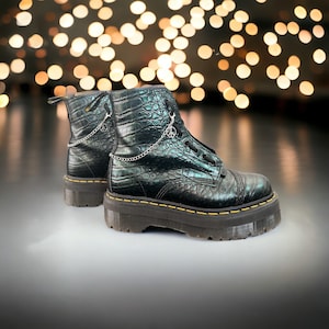 May include: Black leather boots with a crocodile pattern and a yellow stitch detail. The boots have a chunky platform sole and a silver chain with peace sign charms.
