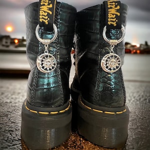 May include: A pair of black leather boots with a crocodile pattern. The boots have a yellow stitching detail around the sole and a silver charm with a sun and moon design attached to each boot.