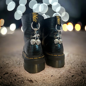 May include: Black leather boots with skull-shaped cherry charms attached to the laces. The boots have a yellow stitching detail and the text "Air Wait" is visible on the laces.