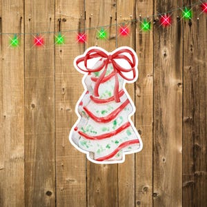 Pode incluir: Uma árvore de Natal branca com listras vermelhas e verdes e um laço vermelho. A árvore é decorada com glitter branco. A árvore está em um fundo de madeira.