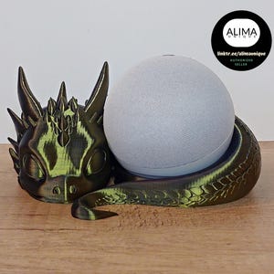 Könnte beinhalten: Ein 3D-gedruckter Drachenkopf-Ständer für einen intelligenten Lautsprecher. Der Drache ist grün und schwarz mit einer strukturierten Oberfläche. Der Ständer ist so konzipiert, dass er einen runden intelligenten Lautsprecher hält, der nicht im Lieferumfang enthalten ist.