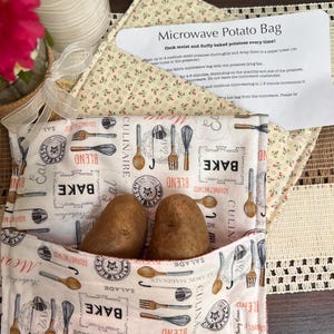 May include: A white microwave potato bag with a culinary-themed pattern, holding two medium-sized potatoes. The bag features illustrations of kitchen utensils and the word "BAKE". A card with instructions is visible.