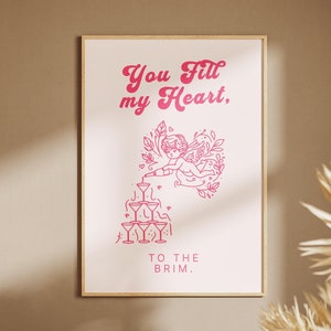 May include: Pink and white printable wall art with a graphic of a cherub pouring champagne into a pyramid of glasses. The text reads "You fill my heart, to the brim."