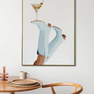 May include: A framed illustration of a pair of light blue cowboy boots with a martini glass resting on top. The martini glass has a green olive garnish.