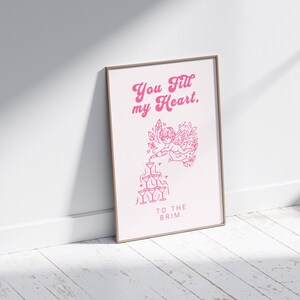 May include: A pink and white printable art print with a graphic of a cupid pouring champagne into a stack of glasses. The text reads "You fill my heart, to the brim."