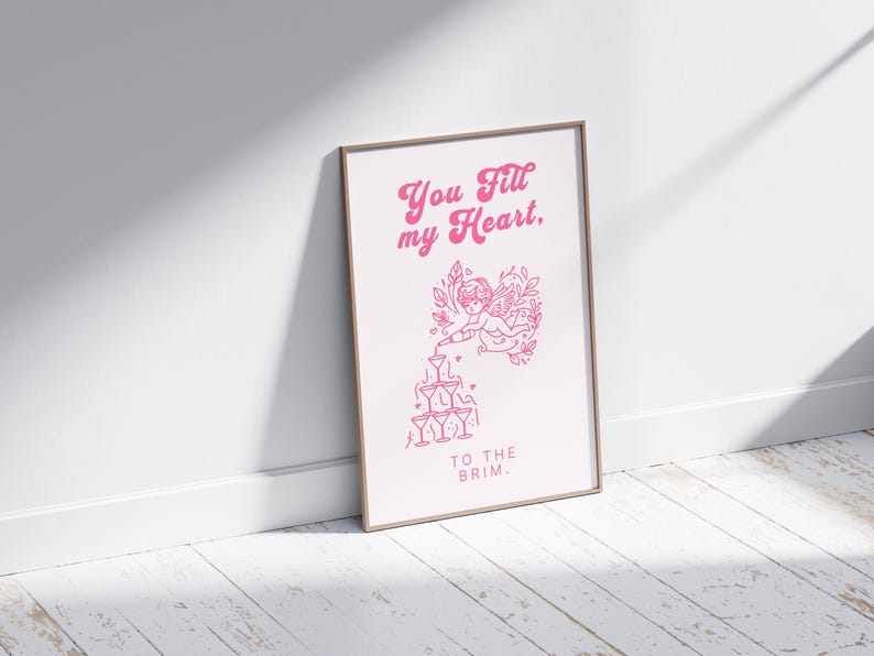 May include: A pink and white printable art print with a graphic of a cupid pouring champagne into a stack of glasses. The text reads "You fill my heart, to the brim."