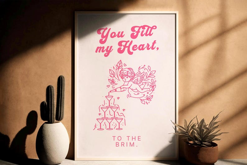 May include: Pink and white printable wall art with a graphic of a cupid pouring liquid into a stack of martini glasses. The text reads "You fill my heart, to the brim."