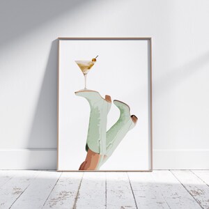 Pu&ograve; includere: Un'illustrazione incorniciata di un paio di stivali da cowboy verdi che tengono un bicchiere da martini con un'oliva come guarnizione.