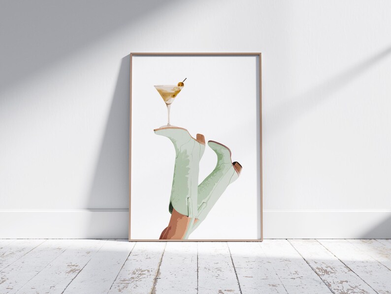 Pu&ograve; includere: Un'illustrazione incorniciata di un paio di stivali da cowboy verdi che tengono un bicchiere da martini con un'oliva come guarnizione.
