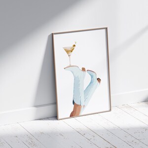May include: A framed watercolor painting of a pair of light blue cowboy boots with a martini glass resting on top. The boots are angled and the glass is tilted slightly.