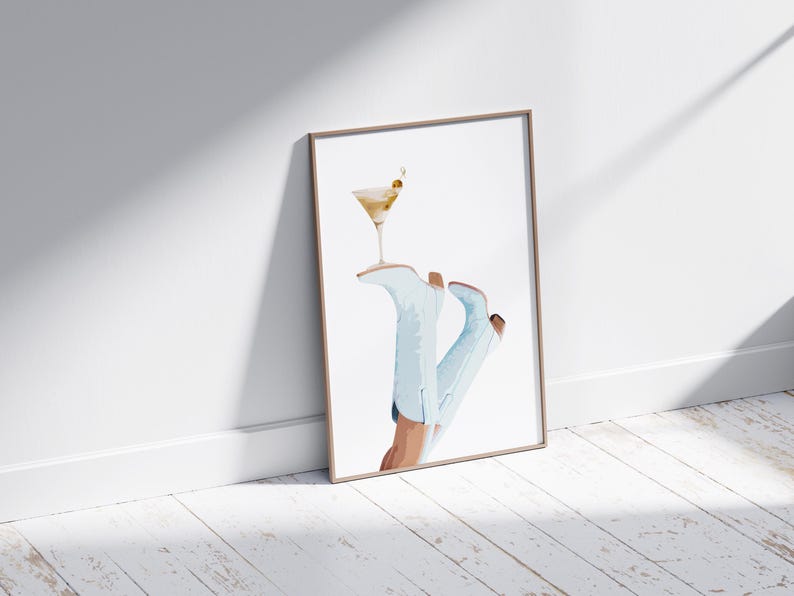 May include: A framed watercolor painting of a pair of light blue cowboy boots with a martini glass resting on top. The boots are angled and the glass is tilted slightly.