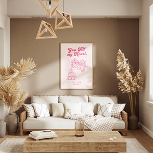 May include: A living room interior with a light brown couch, a wooden coffee table, and a framed print on the wall. The print features a pink graphic with the text "You fill my heart. To the brim."