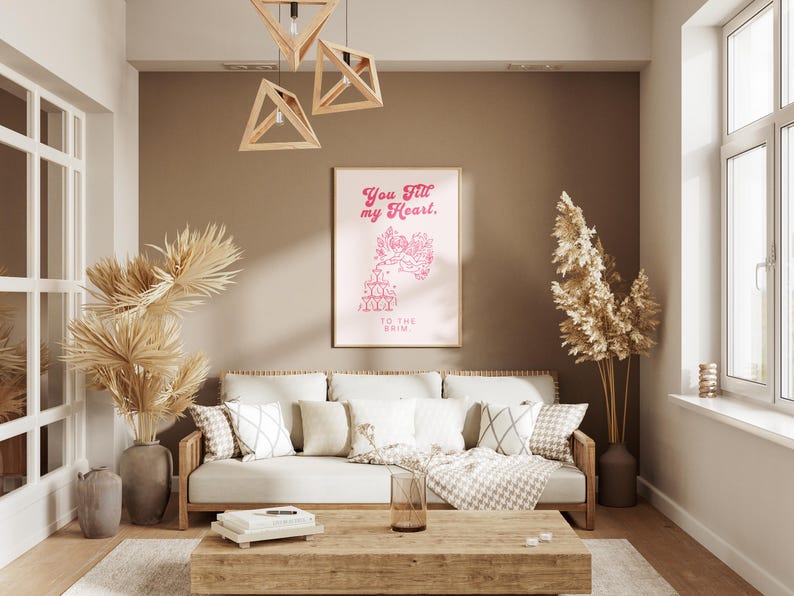May include: A living room interior with a light brown couch, a wooden coffee table, and a framed print on the wall. The print features a pink graphic with the text "You fill my heart. To the brim."