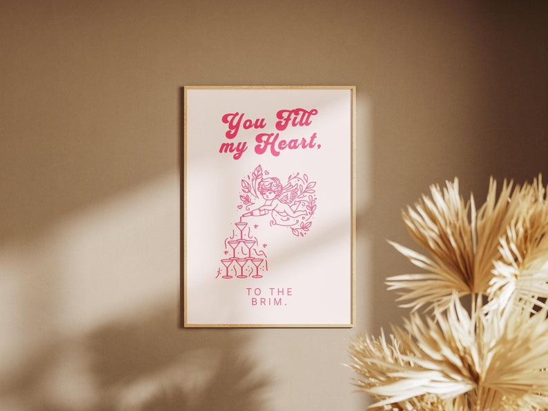 May include: Pink and white printable wall art with a graphic of a cherub pouring champagne into a pyramid of glasses. The text reads "You fill my heart, to the brim."