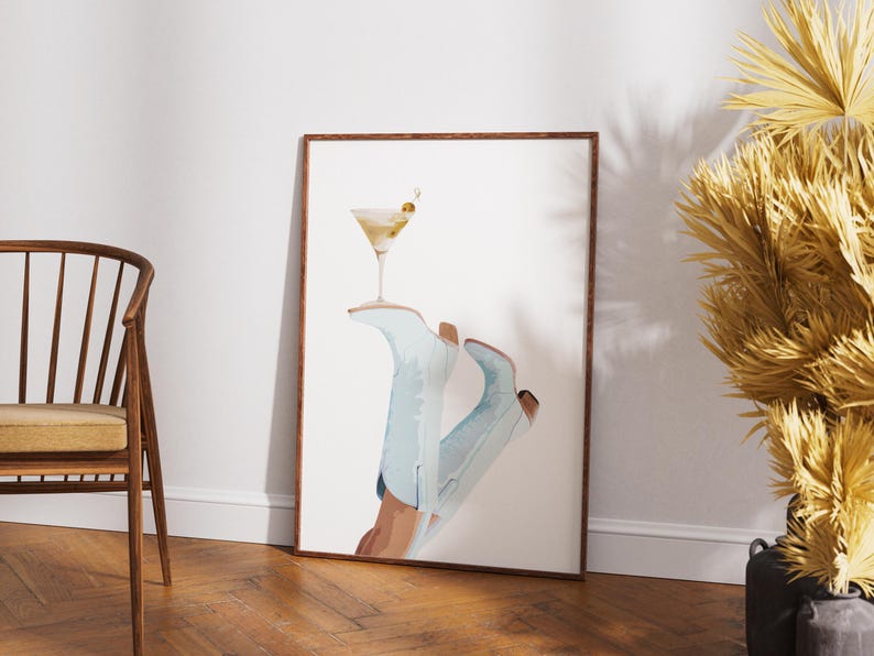 May include: A framed print of a pair of blue cowboy boots with a martini glass on top. The boots are tilted at an angle, and the martini glass is filled with a clear liquid and a green olive.
