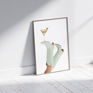 Pu&ograve; includere: Un'illustrazione incorniciata di un paio di stivali verdi con un bicchiere da martini in cima. Gli stivali sono in stile acquerello e lo sfondo &egrave; bianco.
