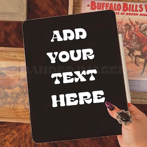 May include: Black iPad with a white sticker that says "ADD YOUR TEXT HERE" in a retro font. The iPad is on a wooden surface.