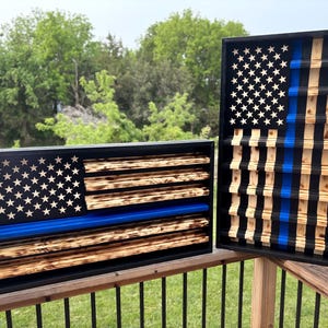 May include: Two wooden American flag wall art pieces. One is rectangular, the other is vertical. Both feature the stars and stripes design with a blue stripe. The wood has a burnt finish, and the stars are white.