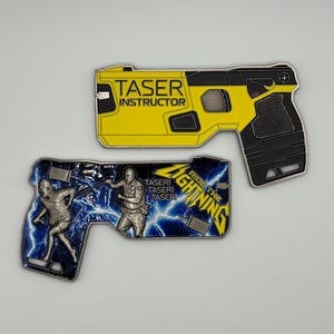 May include: Two metal pins in the shape of a Taser gun. One is yellow and black with the text "TASER INSTRUCTOR". The other is blue and silver with the text "RIDE THE LIGHTNING".