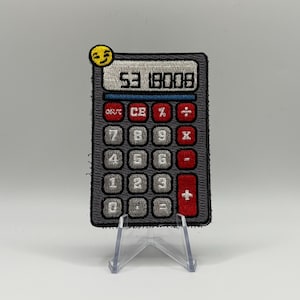 May include: A gray embroidered patch of a calculator with a red plus sign button. The calculator display shows "53 18008". A yellow smiley face is above the calculator.