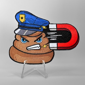 May include: Embroidered patch featuring a cartoon poop character wearing a police hat and holding a magnet. The poop has an angry expression with blue eyes and a white, clenched mouth. The magnet is red and black.