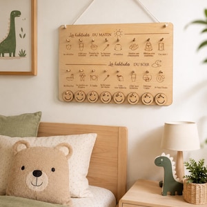 May include: A wooden chore chart with the text "Les habitudes DU MATIN" and "Les habitudes DU SOIR" is hanging on a wall. The chart has icons and pegs for morning and evening routines. A framed dinosaur print, a bear pillow, and a green dinosaur figurine are also visible.
