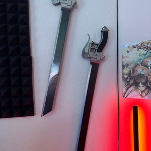 May include: Two silver-colored swords with black handles are mounted on a white wall. The swords have a unique design with a curved handle and a blade that is slightly curved.