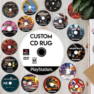 May include: A custom CD rug with a central disc design and the text "CUSTOM CD RUG." The rug features various video game discs, including "Minecraft," "Call of Duty," and "Mortal Kombat." The discs are arranged on a light wood surface. The PlayStation logo is also visible.