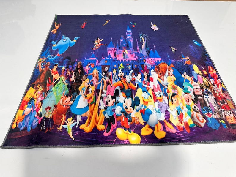 May include: A vibrant blanket displaying a collage of Disney characters in front of a castle. The blanket features characters from various Disney films, including Mickey Mouse, Donald Duck, and others, set against a dark purple backdrop.