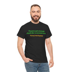 May include: Black t-shirt with the text "They've got enough cheek for a second arse. Funny Irish Sayings" in green and gold lettering. The shirt is worn by a person with a beard and blue jeans.