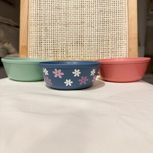 Puede incluir: Tres cuencos, uno verde, uno azul con flores rosas y uno rosa. Los cuencos están sobre una superficie blanca.