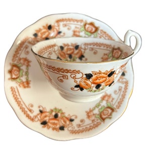 May include: A white teacup and saucer set with a floral pattern in shades of orange, brown, and black. The floral design features stylised flowers and leaves.