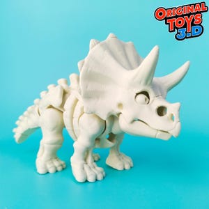 Puede incluir: Un modelo de esqueleto de dinosaurio de plástico blanco, que representa un Triceratops. El dinosaurio tiene una gran gola en la cabeza y tres cuernos. El juguete está articulado y se puede colocar en diferentes posiciones. El juguete está hecho por Original Toys 3-D.