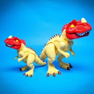 Puede incluir: Dos juguetes de dinosaurio amarillos con cabezas rojas. El dinosaurio más grande está de pie sobre sus cuatro patas, mientras que el dinosaurio más pequeño está de pie sobre dos patas. Ambos dinosaurios tienen dientes y garras afiladas.
