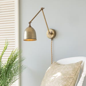 May include: A vintage-style brass wall lamp with an adjustable arm and a domed shade. The lamp is fixed to a pale blue wall. A patterned cushion sits on a white chair, creating a cozy atmosphere.
