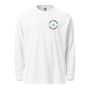 以下が含まれることがあります： 白い長袖Tシャツ、クルーネック。 シャツの左胸上部に「TRUE NORTH SEEK JESUS」の文字と緑色のコンパスローズをあしらった円形デザインが施されています。