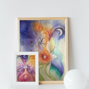 Pode incluir: Duas pinturas de aquarela emolduradas, uma com um design abstrato colorido e a outra com um design mais detalhado que apresenta um olho estilizado e a palavra "ART" no centro. As pinturas estão sobre uma superfície branca com um orbe branco em primeiro plano.