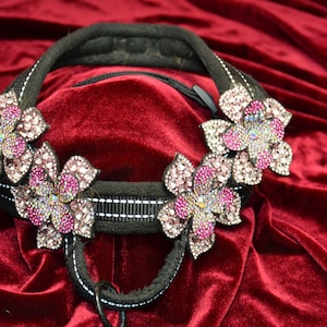 May include: A black dog collar with three pink and silver flower-shaped embellishments. The collar is made of a soft, padded material and has a silver metal buckle.