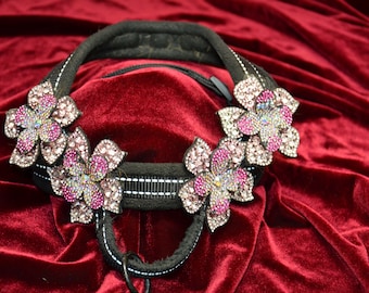 Puede incluir: Un collar de perro negro con tres adornos en forma de flor rosa y plata. El collar está hecho de un material suave y acolchado y tiene una hebilla de metal plateado.