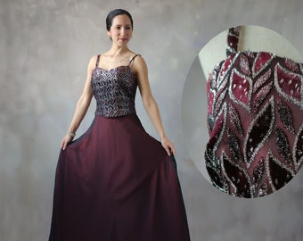 May include: A burgundy and black formal gown with a silver and black sequined bodice and a flowing skirt. The bodice has a sweetheart neckline and is adorned with a delicate floral pattern.