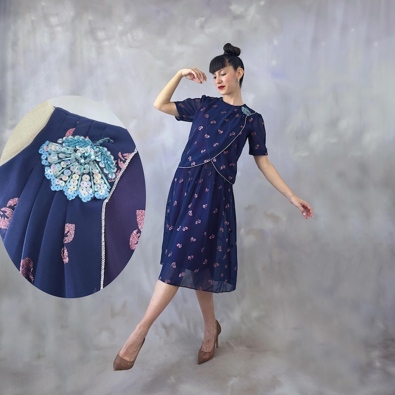 Dreamy ocean blue chiffon dress from the 70s with pink glitter leaf print and light blue sequin appliqué on the chest. Silver-trimmed wrap bodice, round neckline, short transparent sleeves with pearl detail, and an A-line midi skirt with soft pleats at the waist. Fully lined in burgundy satin. A romantic and timeless piece in flawless vintage condition. Recommended for small to medium sizes.