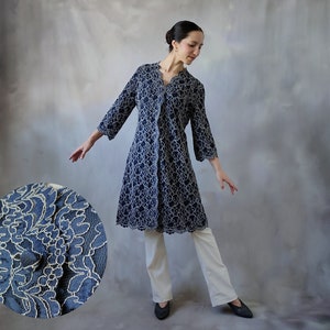 Könnte beinhalten: Eine marineblaue Spitzenjacke mit weißem Blumenmuster. Die Jacke hat einen V-Ausschnitt und lange Ärmel. Das Model trägt die Jacke zu einer weißen Hose und schwarzen Schuhen.