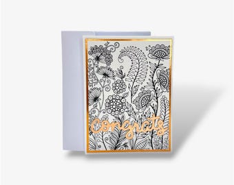 May include: A rectangular greeting card featuring a black and white intricate floral pattern with a metallic gold border. The word "congrats" is written in a metallic gold script font across the lower center of the card, which is paired with a plain white envelope.